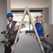 man and woman wearing hard hats standing with a ladder between them inside a room that is under renovation
